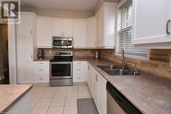 Kitchen featuring white cabinetry, stone-look countertops, stainless steel appliances, a stacked stone backsplash, and tile flooring - 