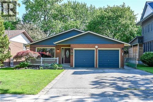 Brick and siding exterior featuring a two-car garage with blue doors, a front lawn, mature landscaping, and a porch with white railing - 25 Inverness Avenue, Hamilton, ON 