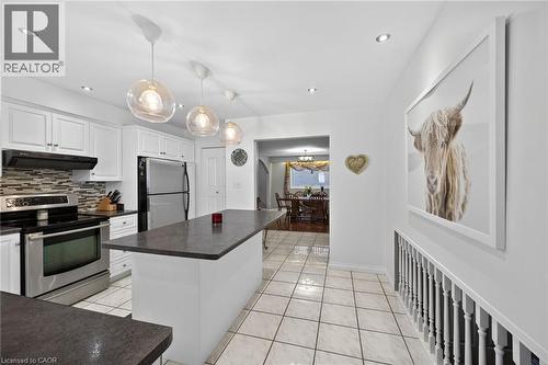 Bright kitchen featuring white cabinetry, stainless steel appliances, a center island with countertop, tiled flooring, and pendant lighting - 25 Inverness Avenue, Hamilton, ON 