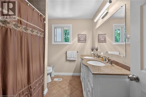 Bathroom featuring a double vanity with integrated sinks, granite-finish countertop, and white cabinetry - 25 Inverness Avenue, Hamilton, ON 