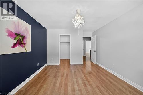 Expansive room featuring light wood-finish flooring, a contemporary ceiling light fixture, and a deep blue accent wall - 25 Inverness Avenue, Hamilton, ON 