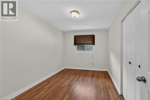 Room featuring wood-finish flooring, neutral wall paint, white trim, a single window, and a built-in closet with bi-fold doors - 25 Inverness Avenue, Hamilton, ON 