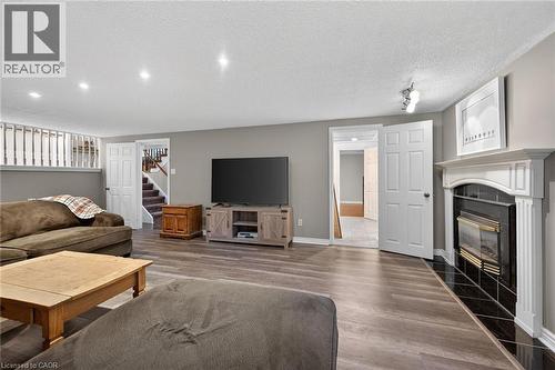 Expansive recreation room featuring wood-finish flooring and a white mantel fireplace with black tile surround - 25 Inverness Avenue, Hamilton, ON 
