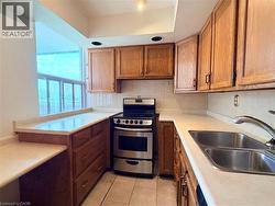 Kitchen featuring wood cabinetry, light-toned countertops, a stainless steel range, and a double basin sink - 