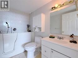 Bathroom featuring a walk-in tub with a handheld shower, a white vanity with an integrated sink, a large wall-mounted mirror, a two-door cabinet with open shelving, and a toilet - 