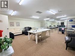 Spacious  craft room featuring carpeted flooring, multiple fluorescent light fixtures, and a neutral wall color - 