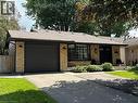Brick facade residence featuring a dark garage door, paved driveway, mature landscaping, and a covered entry with dual dark doors - 39 Forestgate Drive, Hamilton, ON 