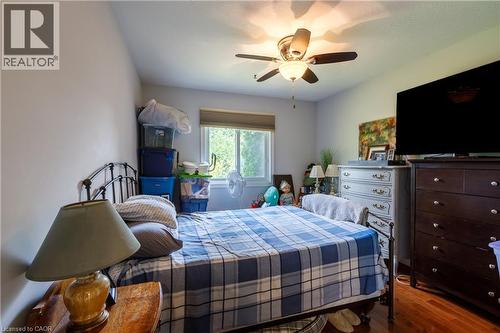 Bedroom featuring wood-finish flooring, a window with a roller shade, a ceiling fan with integrated lighting, and neutral wall tones - 907 Doon Village Road, Kitchener, ON 