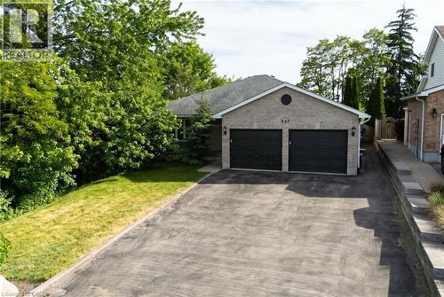 Brick exterior featuring two dark garage doors, a paved driveway, and mature landscaping - 907 Doon Village Road, Kitchener, ON 