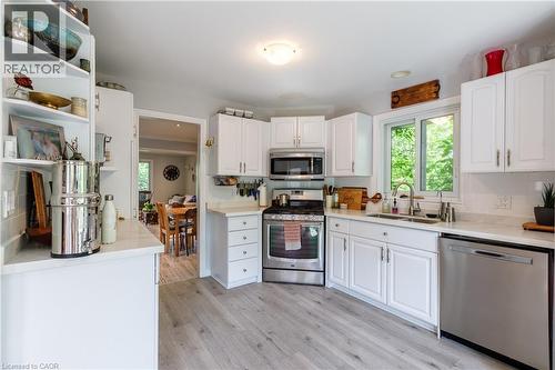 Modern kitchen featuring white cabinetry, light-toned wood-finish flooring, stainless steel appliances, a white subway tile backsplash, and a large window above the sink - 907 Doon Village Road, Kitchener, ON - Indoor Photo Showing Kitchen