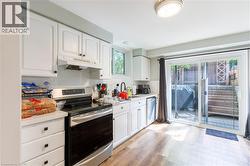 Kitchen featuring white cabinetry, a white subway tile backsplash, stainless steel appliances, wood-finish flooring, and a sliding glass door to exterior - 