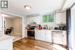 Kitchen featuring white shaker-style cabinetry, wood-finish flooring, stainless steel appliances, a white subway tile backsplash, and a large window above the sink - 