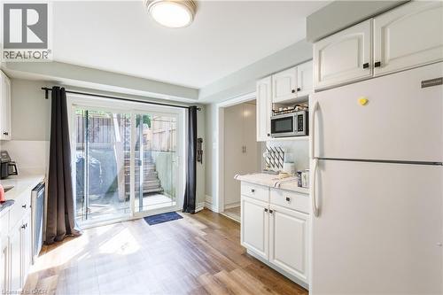 Kitchen area featuring wood-finish flooring, white cabinetry with black hardware, and a sliding glass door - 907 Doon Village Road, Kitchener, ON - Indoor Photo Showing Kitchen