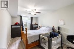 Bedroom featuring wood-finish flooring, a ceiling fan with integrated lighting, and a window with white louvered blinds - 