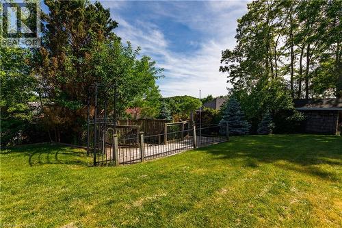 Expansive backyard featuring a large grass lawn, a wood deck with black metal railing, a black metal gate, mature trees, and a wood privacy fence - 907 Doon Village Road, Kitchener, ON - Outdoor