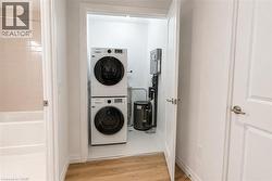 Dedicated laundry area featuring a stacked washer and dryer, adjacent to a bathroom with a white bathtub and neutral-toned wall tiles - 