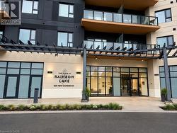Contemporary apartment building entrance featuring a pergola, modern exterior lighting, expansive glass doors, and a concrete walkway - 