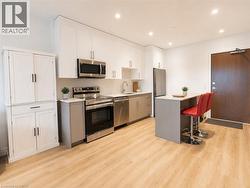 Modern kitchen featuring white upper cabinetry, stainless steel appliances, light wood-finish flooring, a light-toned countertop, and recessed ceiling lighting - 
