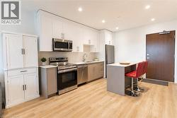 Modern kitchen featuring stainless steel appliances, light wood-finish flooring, white upper cabinetry, and a peninsula with a light-colored countertop - 