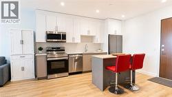 Modern kitchen featuring stainless steel appliances, white upper cabinetry, and a central island with a wood-finish countertop - 