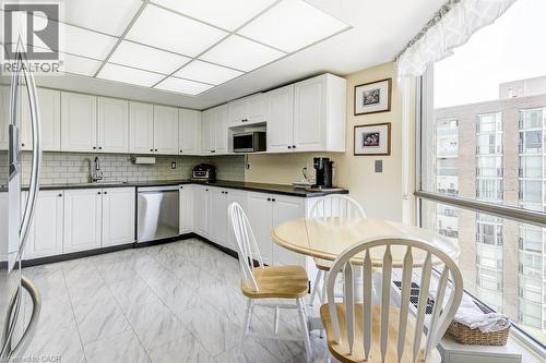 Kitchen featuring white cabinetry, dark countertops, a subway tile backsplash, stainless steel appliances, and large windows - 1201 North Shore Boulevard E Unit# 706, Burlington, ON - Indoor Photo Showing Kitchen