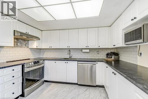 Contemporary kitchen featuring white cabinetry, dark countertops, a subway tile backsplash, stainless steel appliances, and wood-finish flooring - 1201 North Shore Boulevard E Unit# 706, Burlington, ON - Indoor Photo Showing Kitchen