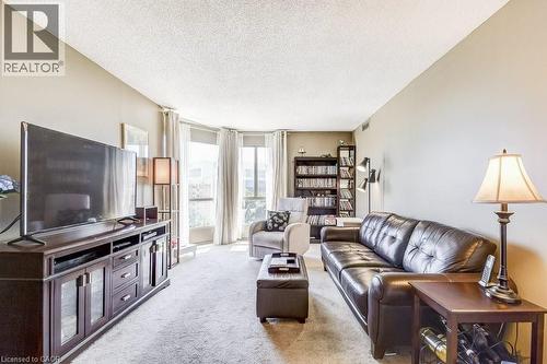 Carpeted living area featuring a wood-finish media console, light-colored walls, and a curved wall of windows - 1201 North Shore Boulevard E Unit# 706, Burlington, ON - Indoor Photo Showing Living Room