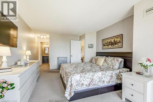 Carpeted room featuring a dark wood bed frame with a built-in headboard, light gray painted walls, and an open doorway revealing a bathroom vanity with a dark wood cabinet - 1201 North Shore Boulevard E Unit# 706, Burlington, ON - Indoor Photo Showing Bedroom