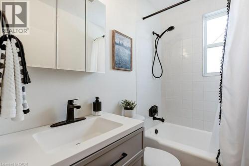 Bathroom featuring a white integrated sink with a matte black faucet, a medicine cabinet with mirrored doors, and a full-size bathtub with white subway tile surround and matte black fixtures - 202 Erindale Avenue, Hamilton, ON 