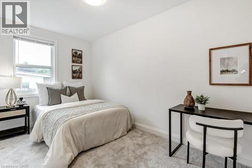 Bright interior space featuring a window with blinds, light-toned wall-to-wall carpeting, crisp white walls, white baseboards, and a flush-mount ceiling light fixture - 202 Erindale Avenue, Hamilton, ON 