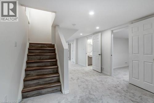 Finished lower level featuring wood-finish stairs, light gray carpeting, recessed lighting, white paneled doors, and a partial bathroom with a circular mirror and vanity - 202 Erindale Avenue, Hamilton, ON 
