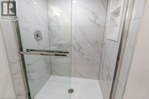 Walk-in shower featuring large format white tiled walls with subtle veining, clear glass enclosure with a chrome towel bar, chrome shower fixtures, and a built-in shower niche - 202 Erindale Avenue, Hamilton, ON 
