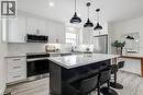 Modern kitchen featuring white shaker cabinetry, a large center island with seating, stainless steel appliances, a white subway tile backsplash, and light wood-finish flooring - 202 Erindale Avenue, Hamilton, ON 