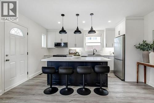 Modern kitchen featuring a large island with dark cabinetry and a light-toned countertop, complemented by three black pendant lights - 202 Erindale Avenue, Hamilton, ON 
