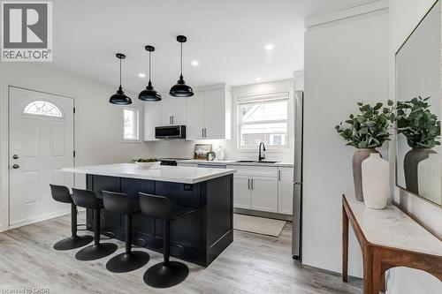 Kitchen featuring a dark-toned island with white countertop, three pendant lights, and light wood-finish flooring - 202 Erindale Avenue, Hamilton, ON 