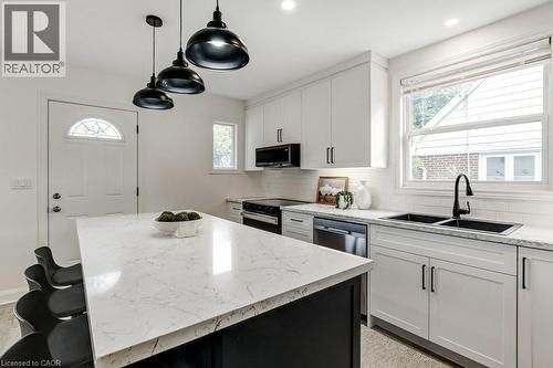 Kitchen featuring a large central island with a light-toned countertop, white cabinetry with matte black hardware, dual black basin sink with a matte black faucet, and stainless steel appliances - 202 Erindale Avenue, Hamilton, ON 