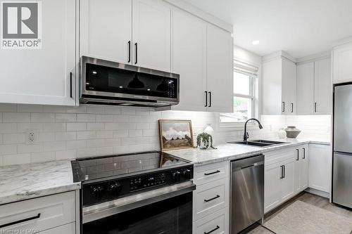 Kitchen featuring white shaker cabinetry with black hardware, stainless steel appliances, light-toned countertops, a white subway tile backsplash, and a black double basin sink with a gooseneck faucet - 202 Erindale Avenue, Hamilton, ON 