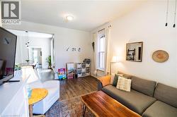 Living area featuring wood-finish flooring, white walls, and a large window with white curtains - 