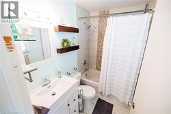 Bathroom featuring a tub/shower combination with tile surround and mosaic accent, white vanity with integrated sink, chrome fixtures, and wood-finish floating shelves - 