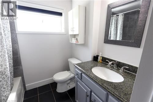 Full bathroom featuring a vanity with a speckled countertop and undermount sink, a framed mirror, a built-in wall cabinet, and dark tile flooring - 77 Orchard Mill Crescent, Kitchener, ON 