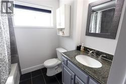 Full bathroom featuring a vanity with a speckled countertop and undermount sink, a framed mirror, a built-in wall cabinet, and dark tile flooring - 