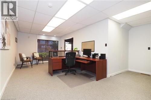 Carpeted interior space featuring a drop ceiling with integrated rectangular lighting panels, white walls, and a large front window - 731 King Street E, Cambridge, ON 