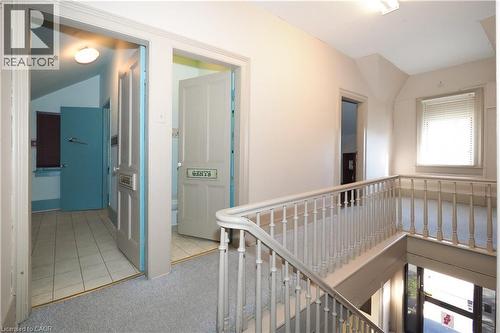 Upper level hallway with carpeted flooring, featuring multiple doorways, a window with blinds, and a staircase with a white spindle railing - 731 King Street E, Cambridge, ON 