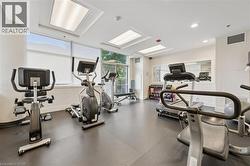 Fitness center featuring multiple exercise machines, recessed lighting, large windows with roller shades, a mirrored wall, and rubber flooring - 