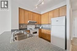 Kitchen featuring granite-look countertops, light wood-finish cabinetry, a double basin stainless steel sink, and a white electric range with matching overhead exhaust hood - 