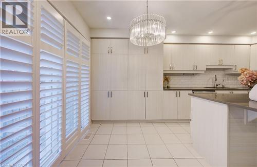 Kitchen with suspended lighting, light tile patterned floors, decorative backsplash, a kitchen bar, and white cabinets - 302 Jean Landing, Milton, ON 