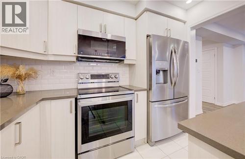 Kitchen featuring stainless steel appliances, decorative backsplash, white cabinetry, light tile patterned floors, and dark stone counters - 302 Jean Landing, Milton, ON 