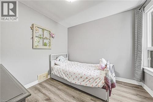 Neutral tone wall paint, wood-finish flooring, white baseboards, and a window with curtains - 47 Fraser Avenue, Hamilton, ON 