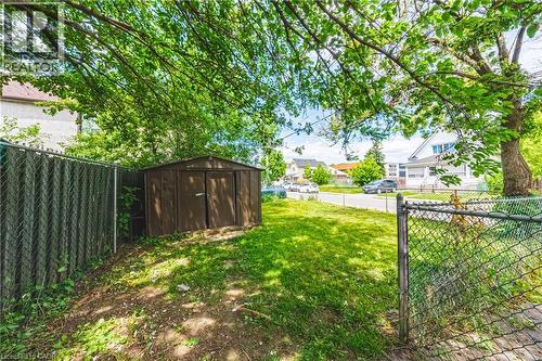 Expansive backyard featuring a brown storage shed, a chain-link fence, and mature trees providing natural shade - 47 Fraser Avenue, Hamilton, ON 