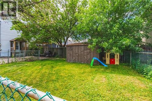 Expansive backyard featuring a green lawn, mature trees, a wooden shed, and chain-link fencing - 47 Fraser Avenue, Hamilton, ON 